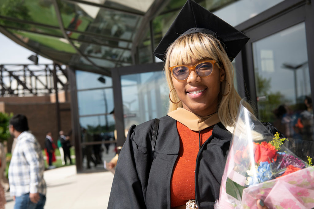 A graduate standing with a bouquet of flowers after commencement