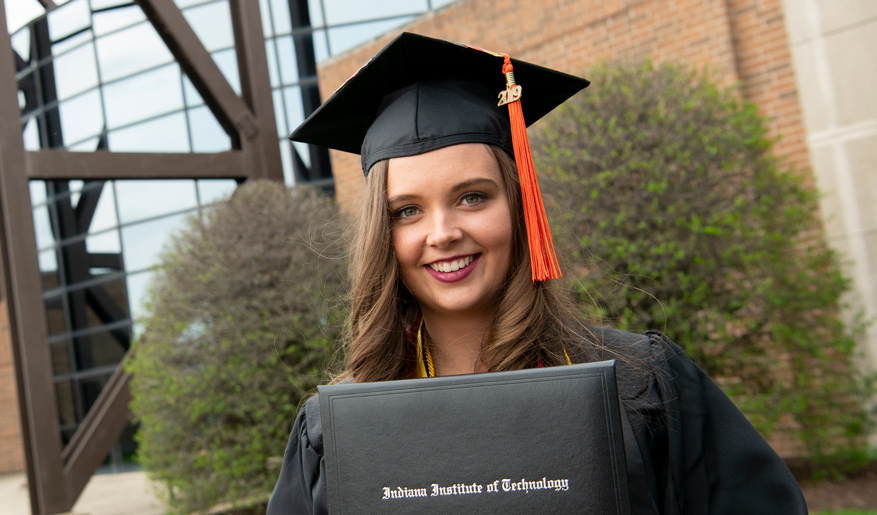 Graduate standing outside as she poses with her Indiana Institute of Technology degree