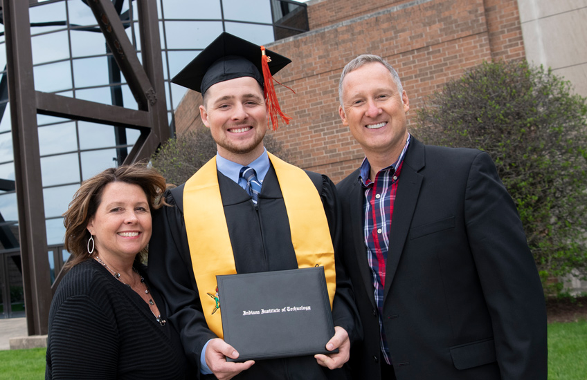 A graduate posing with his family for a photo while holding his degree from Indiana Tech Institute of Technology