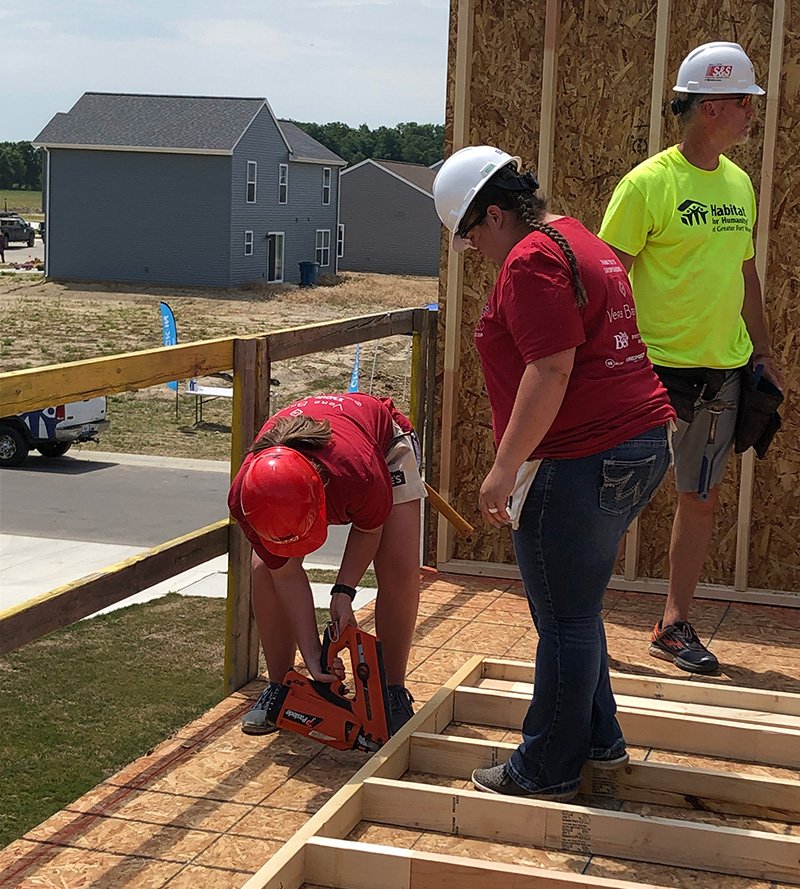 Two women using a nail gun to nail into a house frame 